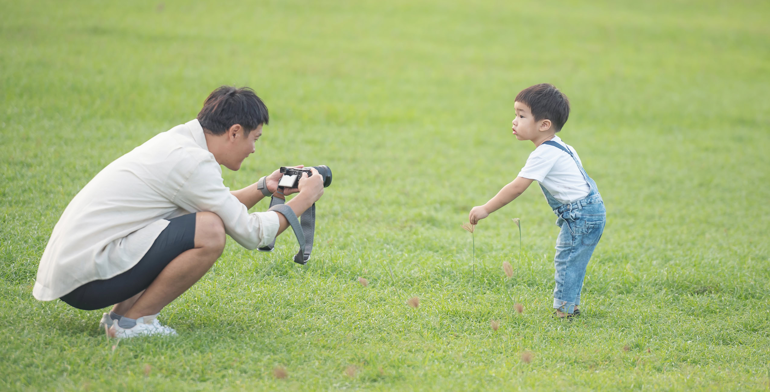 father with digital video camera recording his son portrait happy father son park